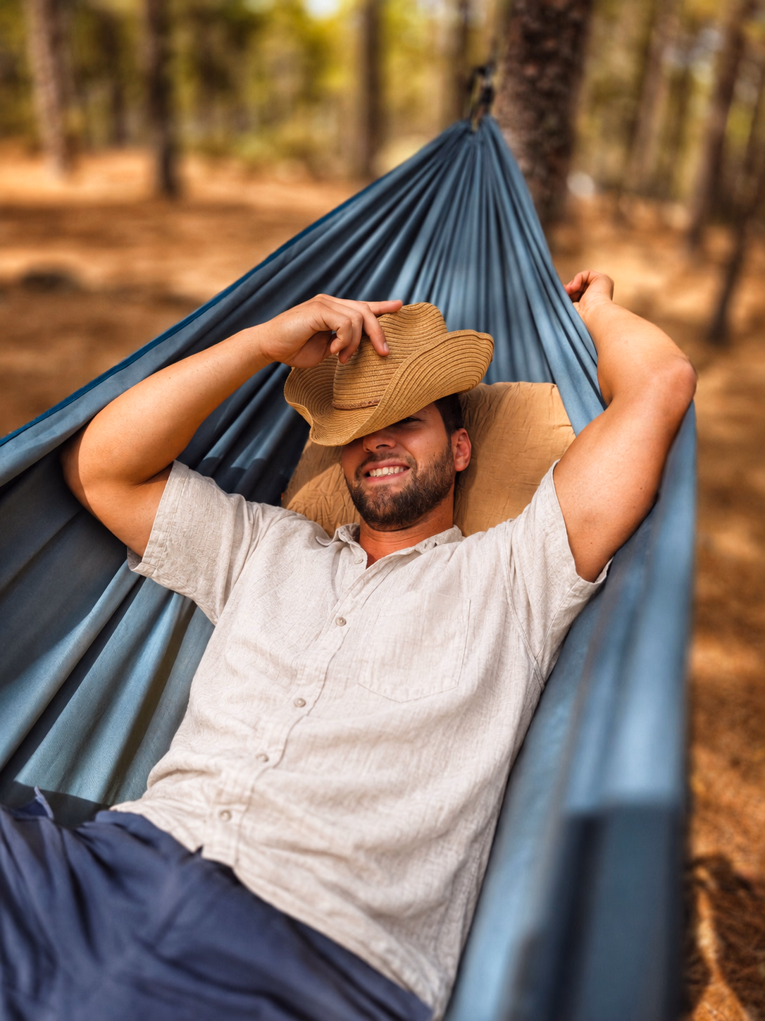 Alexander, companion for couples, lying in a hammock in a pine grove in Gran Canaria, linen shirt and straw hat.