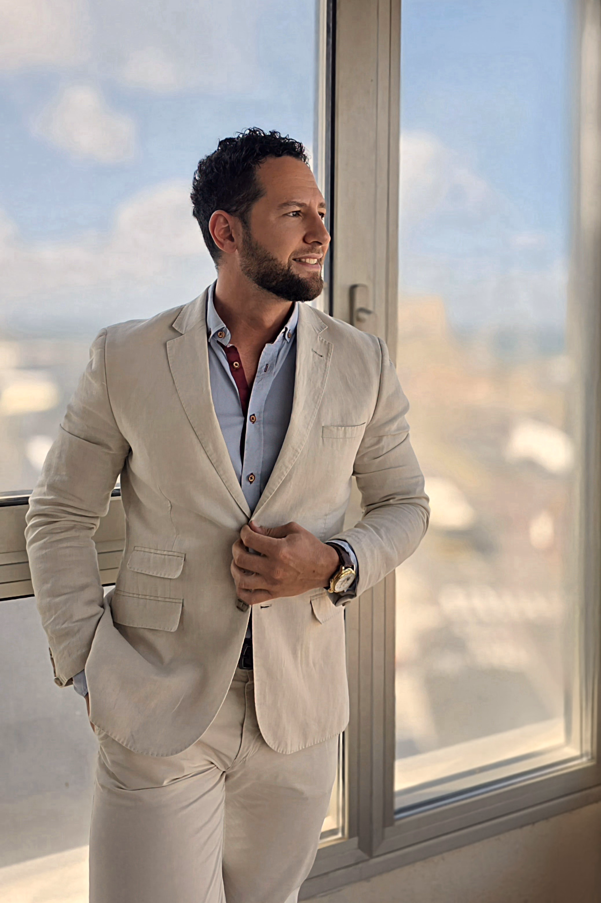 A large window overlooking Las Palmas, Gran Canaria. Alexander in a light linen suit, gentleman companion for women and couples.