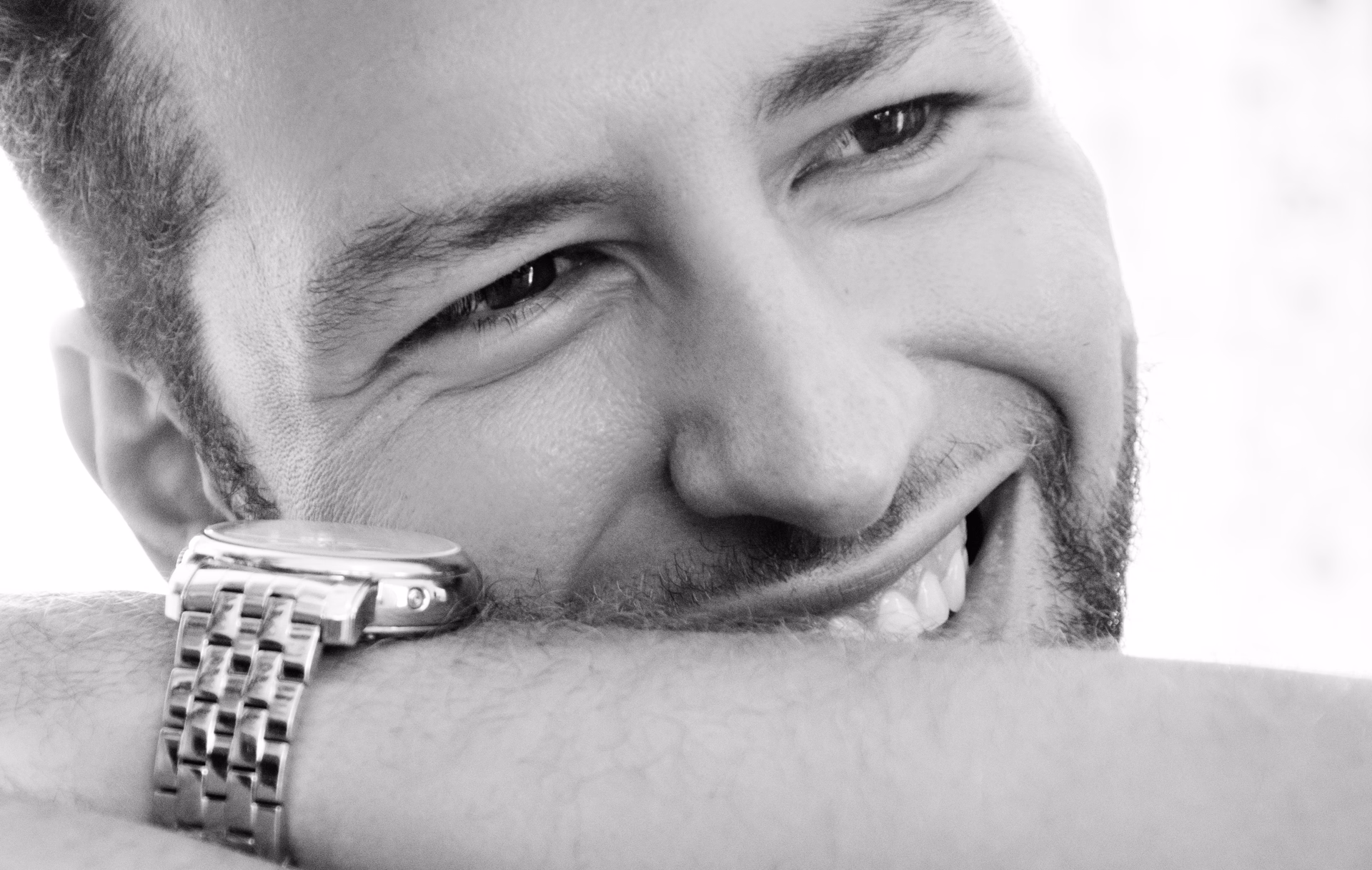 Alexander, escort, in a close black-and-white portrait, smiling with his face resting on his forearm.
