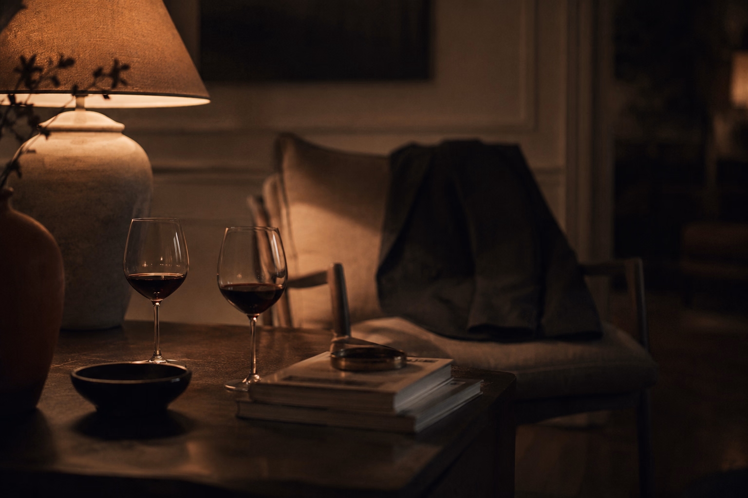 A lamp on a table, two glasses of wine and two jackets over the backs of two chairs: two presences, no faces. The real intimacy that stays off-camera.