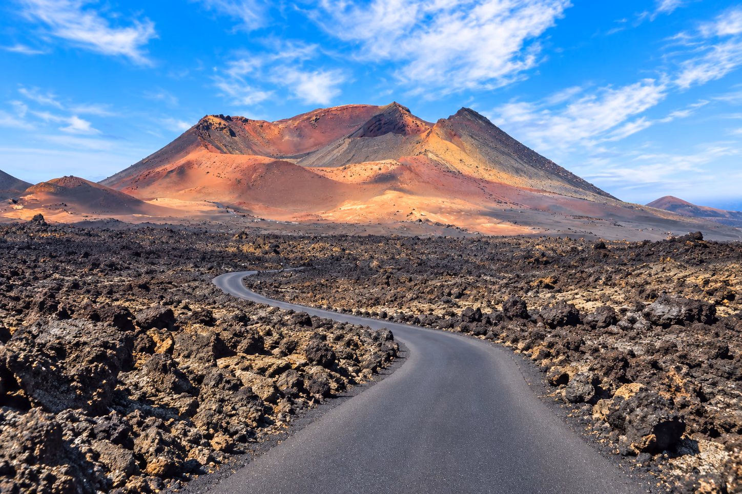 Eine Straße durch die Lavaströme von Timanfaya, auf die roten Vulkane zu